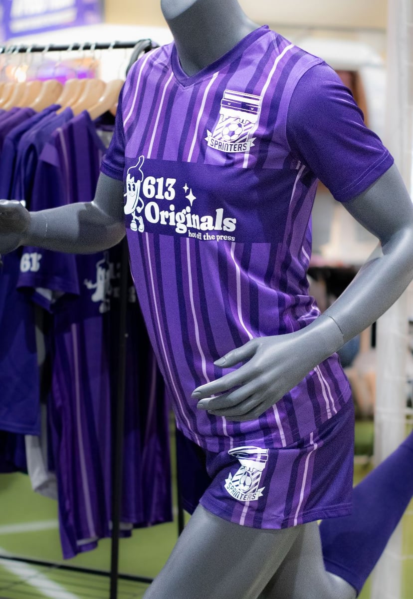 A female mannequin in a running stance wearing a full purple soccer kit decorate with "613 Originals" in all white and a team logo on the shorts and chest.