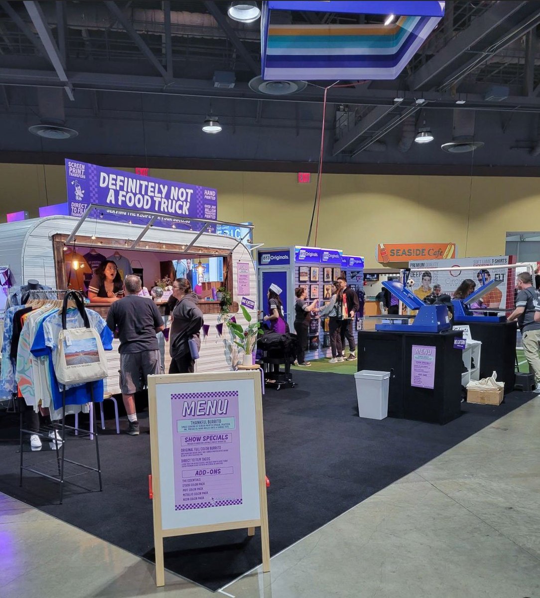 A full look at our booth. A menu board is visible in front with all of the giveaway options. Behind it is our food truck and soccer area. Within the space are mannequins and garment racks.