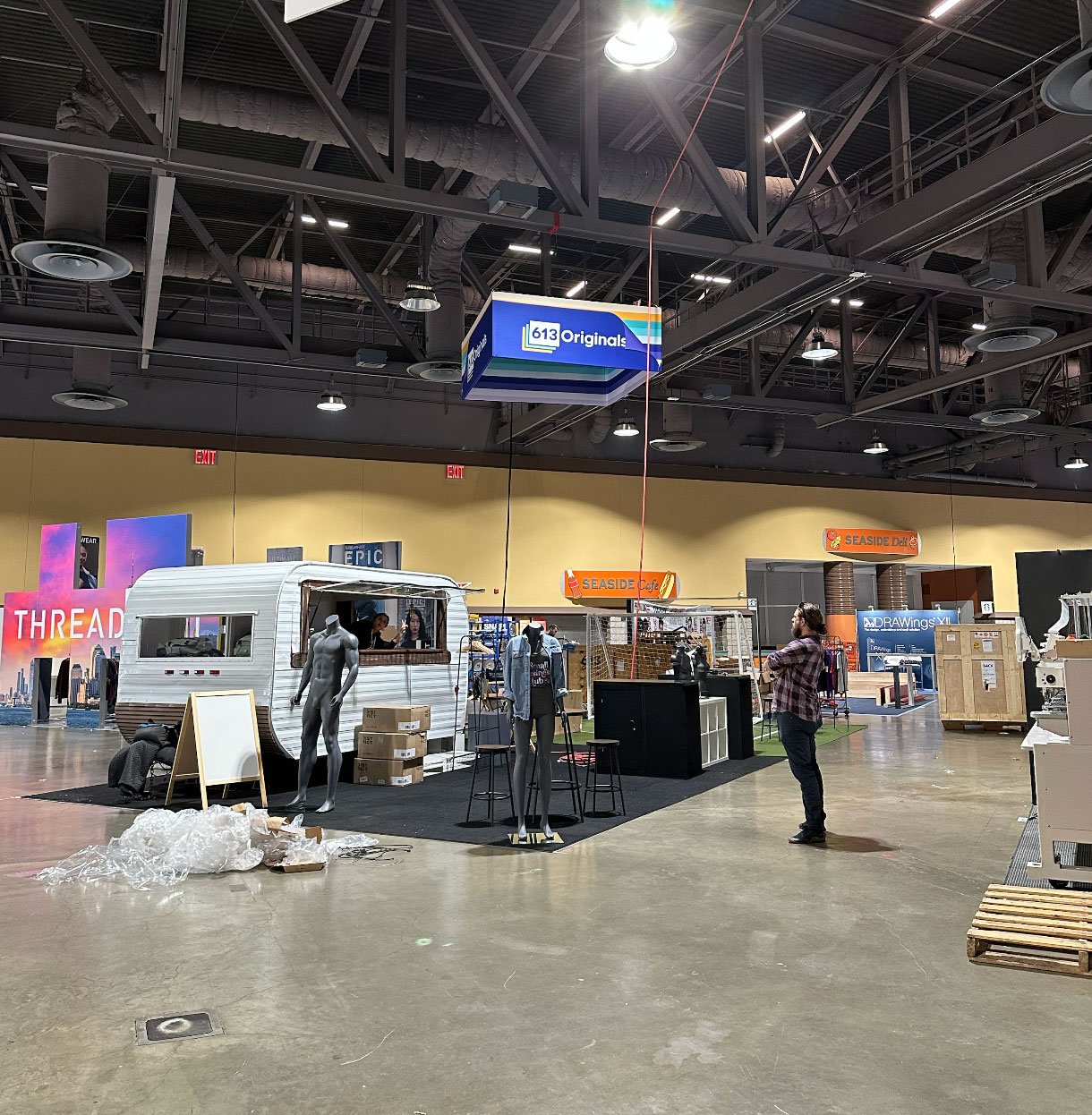 Booth half-assembled. A hanging sign, truck, and various mannequins are visible