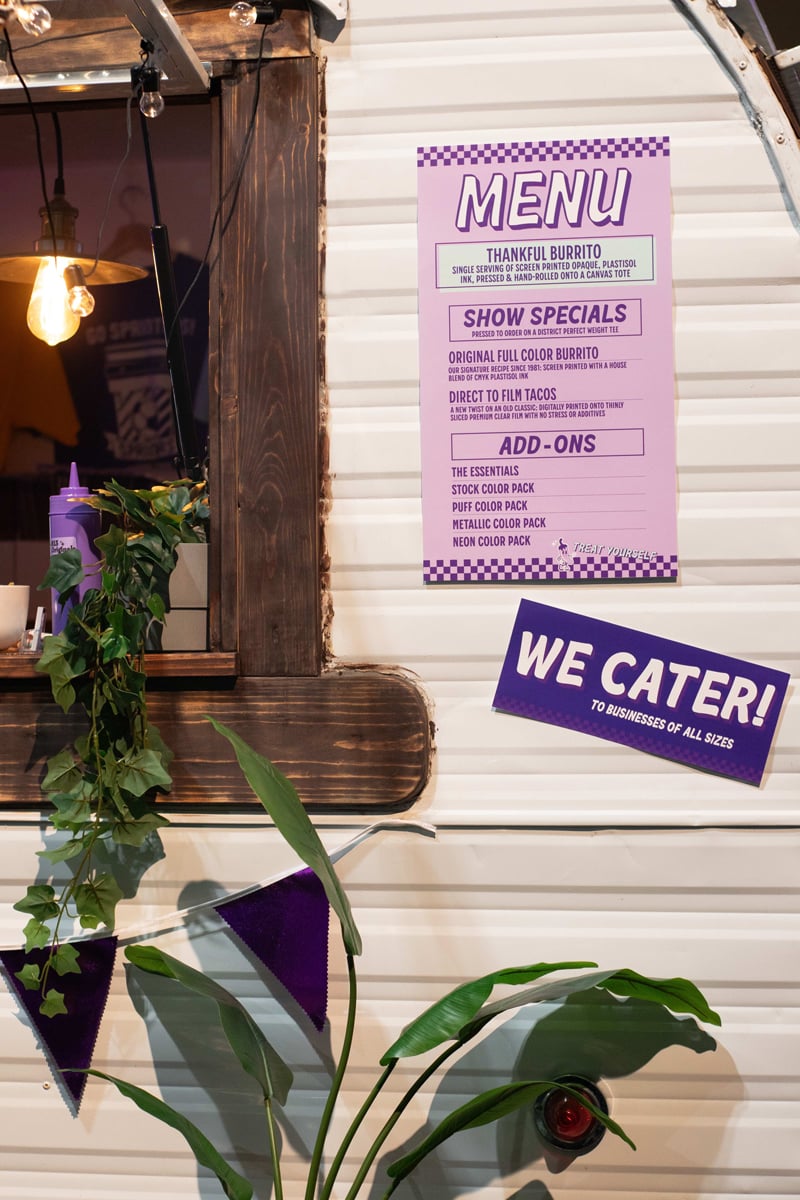 An image of a purple menu on our "food truck" with multiple options. Also seen here is a sign that says "we cater to businesses of all sizes"